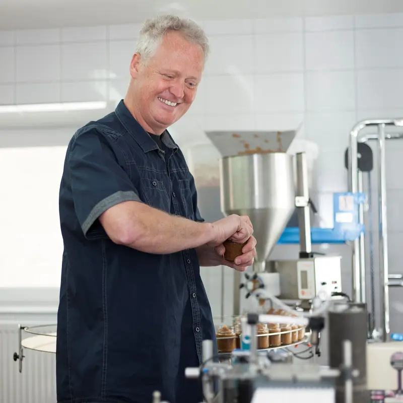 Bernd Troger verschließt lächelnd ein Senfglas in seiner Manufaktur